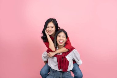 Pembe arka planda eğlenen kadınlar. Koyu saçlı kız arkadaşının arkasından zıplıyor..