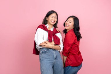 Sıradan giyinmiş çekici lezbiyen çift, stüdyoda pembe arka planda fotoğraf çekerken gülümsüyor ve gülüyorlar..