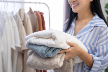 Çamaşır odasında yıkandıktan ve kurulandıktan sonra katlanmış bir yığın elbise tutan güzel bir Asyalı kadın. Ev işi kavramı