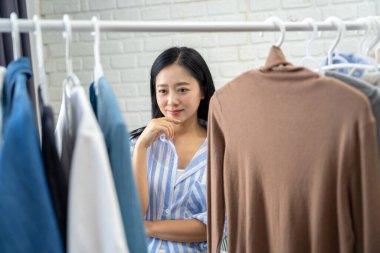 Asian female considering cloth to wear on date night.