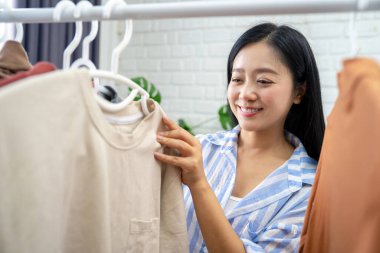 Genç Asyalı kadın tatilde giyecek kıyafet seçiyor.