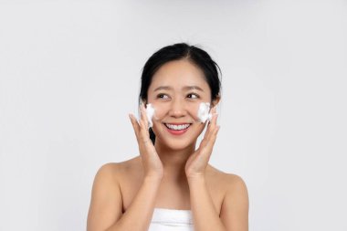 Gülümseyen ve mutlu genç kadın makyajı beyaz arka planda köpükle temizliyor. Cilt bakımı kavramı.