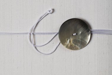 Kumaş bir yüzey üzerinde duran inci düğmenin detaylı bir yakın çekimi. Düğmelerin parlak dokusu ışığı yansıtır, yanardöner kalitesini gösterir..