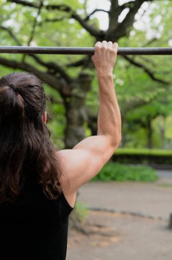 Kentteki yeşil yapraklı parktaki metal çubukta barfiks çeken kişi..