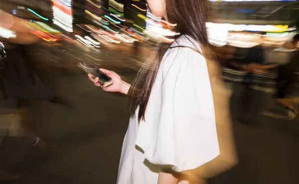 Canlı bir gece kalabalığında beyaz elbiseli bir kadın elinde telefon tutuyor..