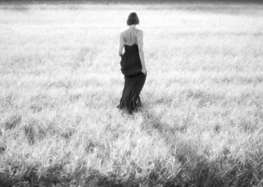 Parlak otlakta tek başına yürüyen bir kadının arka görüntüsü..