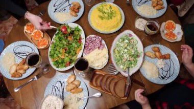 Çeşitli lezzetli yemeklerle dolu bir yemek masasının üst görüntüsü. Tanınmayan insanların elleri tabaklarına yemek döküyor...