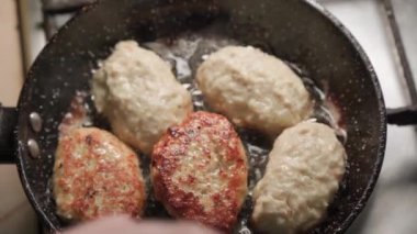 Cooking meat cutlets in a frying pan with boiling oil in a home kitchen. A woman's hand turns them over..