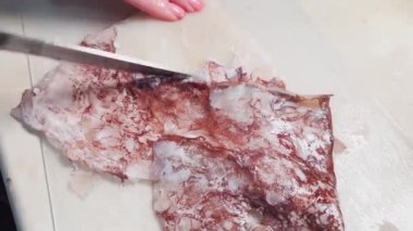 Women's hands remove the skin from the squid before cooking it..