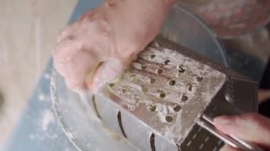 Women's hands rub butter with a grater, close-up.