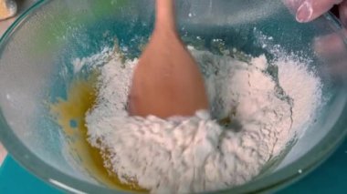 Kneading the dough in a glass bowl with a wooden spatula.