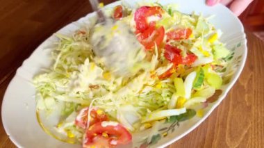 Mixing salad with fresh vegetables, tomatoes, peppers, cucumbers, cabbage, and eggs using a spoon.