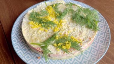 A woman is garnishing a just-made Mimosa salad by sprinkling it with yellow egg yolk.