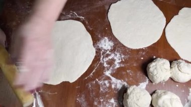 Kadınların elleri, ev yapımı ekmek yaparken merdaneyle hamuru yuvarlıyor..