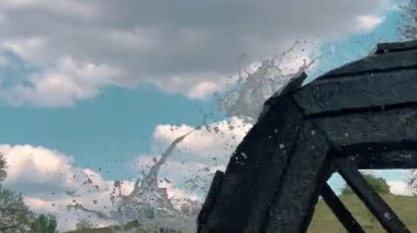 Su değirmeninin çarkının hareket halindeki su damlaları mavi gökyüzüne karşı farklı yönlere uçuyor..