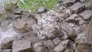 Şelaleden düşen su damlaları gri taşlara düşer ve farklı yönlere uçar..