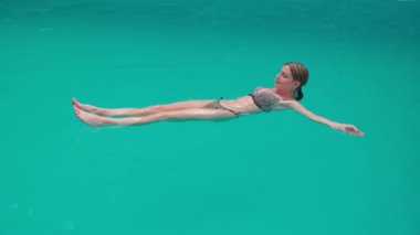 Genç bir kadın havuzun yüzeyinde yatıyor..
