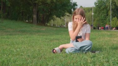 Parktaki çimlerin üzerinde oturan sevimli bir kız. Hikayeler ya da yayınlar internette canlı yayında..