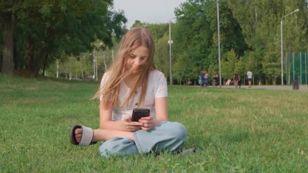 Молодая Девушка Сидящая Траве Парке Просматривает Социальные Сети Смартфоне — стоковое видео