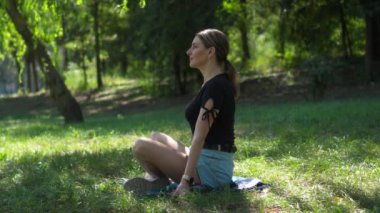 Genç kadın ağaçların gölgesinde yeşil çimlerde oturur. Rahatlamayı ve temiz havayı sever, koşuşturma ve koşuşturmadan uzakta..