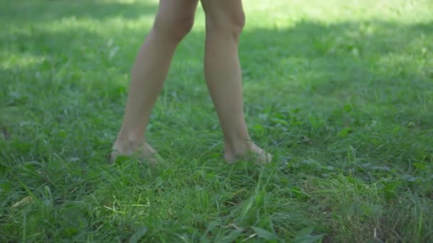女性の細い足は緑の草の上に裸足を歩きます — ストック動画