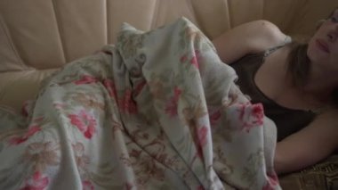 Orta yaşlı bir kadın kanepeye uzanırken battaniyeye sarılmış..