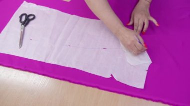 Atölyedeki terzi, kağıt şablonu kullanarak gelecekteki elbise için işaretler yapıyor..