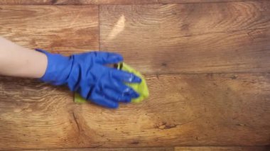 Eldiven giymiş bir kadının eli temizlik sırasında zemini paçavrayla siler..