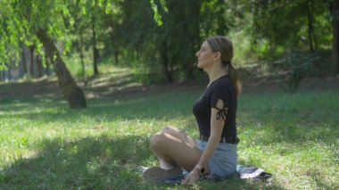 Orta yaşlı bir kadın yeşil bitki örtüsünün arasında parkta dinleniyor. Hafif serinletici esintiden hoşlanıyor..