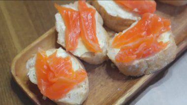 Tahtanın üzerinde beyaz tereyağlı ekmek ve kırmızı balıklı sandviçler var..