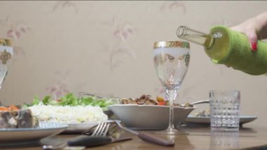 Kadının eli yemek masasında duran beyaz şarabı cama döküyor..