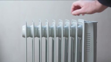 Adamın eli elektrikli ısıtma radyatörünün ısısını kontrol ediyor..