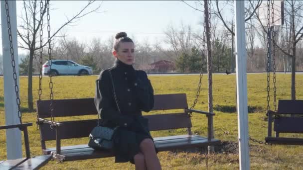 孤独而时尚的女人坐在公园的长椅上 一个人无聊地四处张望 — 图库视频影像