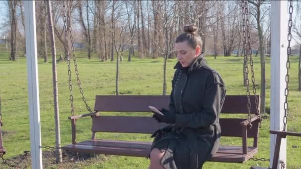 女人坐在秋天公园的长椅上 看着她的智能手机 — 图库视频影像