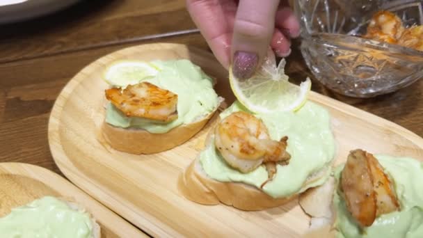 一个女人的手在餐桌上用鳄梨和虾仁装饰三明治 加入柠檬片 — 图库视频影像