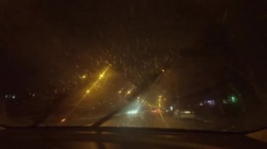 View through windshield of car at night during snowfall.