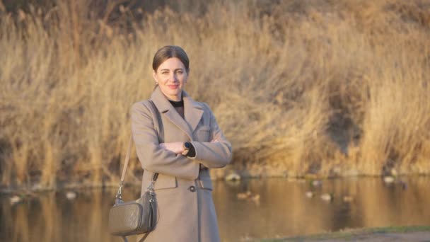 有魅力的中年妇女穿着米黄色外套 面对着湖中鸭子的背景 看着相机 — 图库视频影像