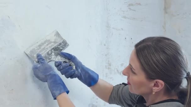 女人在装修房间 她用铲子把墙上的旧油灰刮掉 — 图库视频影像