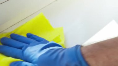 Mavi kauçuk eldiven, temizlik yaparken sarı bez tozunu siler...
