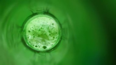 Soyut yeşil arka plan, cam şişenin dibinde köpüklü içecek var...