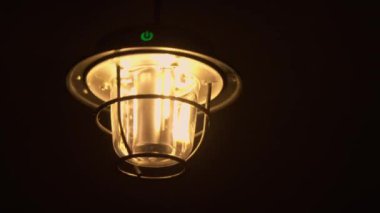 Ilık ışığı olan bir lamba Karanlıkta rüzgarda sallanıyor..