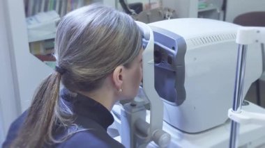 Klinikte otomatik refraktometreyle göz muayenesine giren bir kadın...