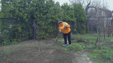 Turuncu kazaklı yaşlı bir kadın arka bahçede çalışıyor..