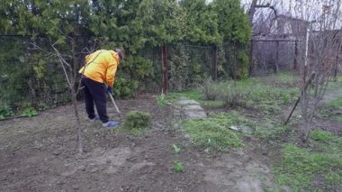 Turuncu kazaklı yaşlı bir kadın arka bahçede çalışıyor..