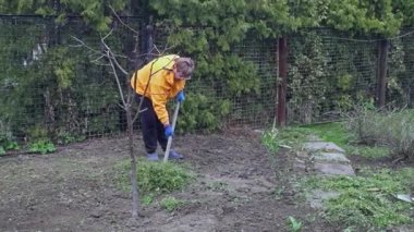 Bahçedeki bitkileri temizleyen turuncu kazaklı yaşlı bir kadın..