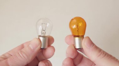 Ellerinde iki farklı araba ampulü var: biri temiz, diğeri turuncu..