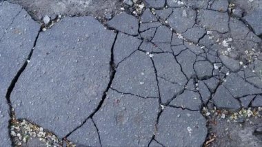 Çatlamış asfalt yüzeyinde birden fazla çatlak var. Aşınmayı ve zamanın etkilerini sembolize ediyor..