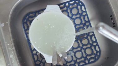 Su musluktan lavaboya akıyor deterjan köpüğüyle kaplanmış kirli tabaklarla..