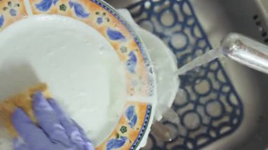 Eldivenli bir el köpüklü suyun altında kirli bulaşıkları süngerle yıkar..