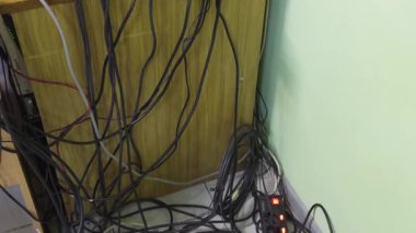 Elektrik kablolarının karışıklığı bir güç şeridine bağlı, düzensiz bir şekilde duvara saçılmış, kaotik bir görünüm yaratıyor..